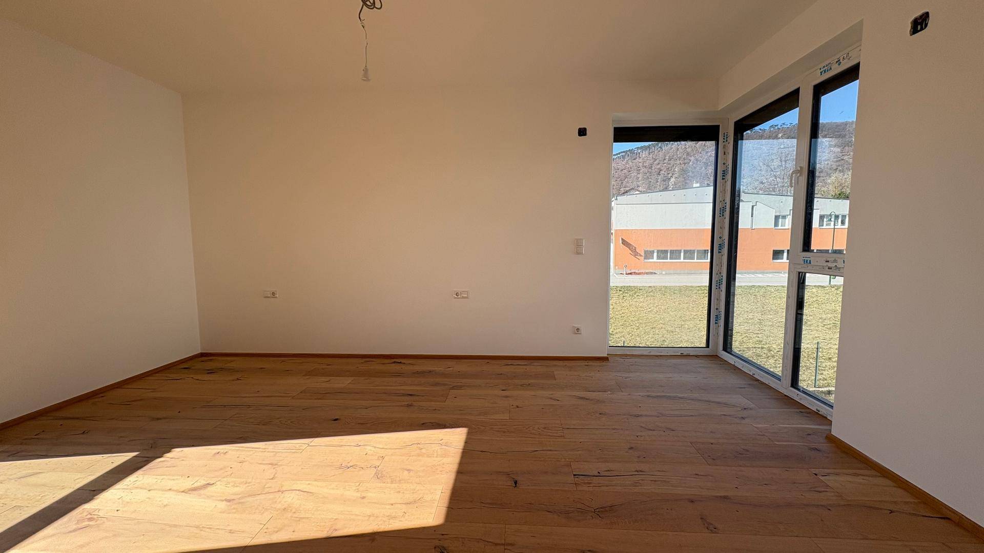 Helles, unmöbliertes Zimmer mit Holzboden und großen Fenstern, bereit zur individuellen Einrichtung.