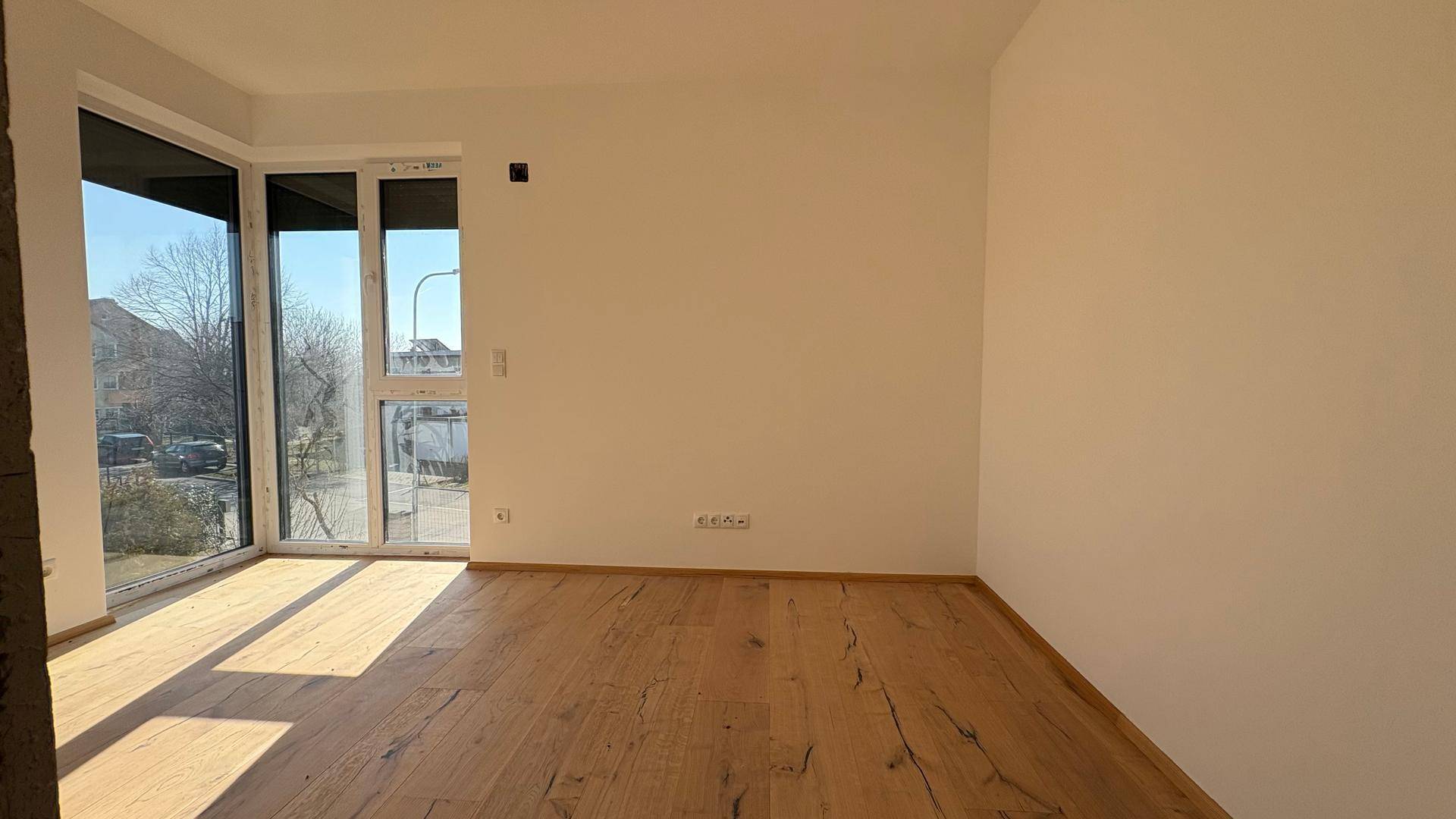 Geräumiges, unmöbliertes Zimmer mit Holzboden und großen Fenstern, ideal als Schlaf- oder Arbeitszimmer.