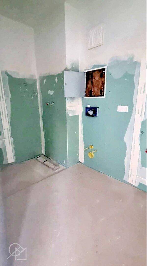 Badezimmer im Rohbau mit vorbereiteten Anschlüssen für Toilette und Waschbecken.
