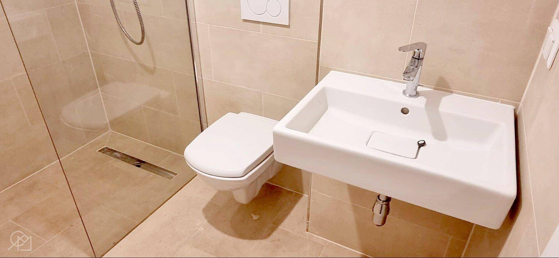 Modernes Badezimmer mit beigefarbenen Fliesen, ebenerdiger Dusche und wandhängendem WC.