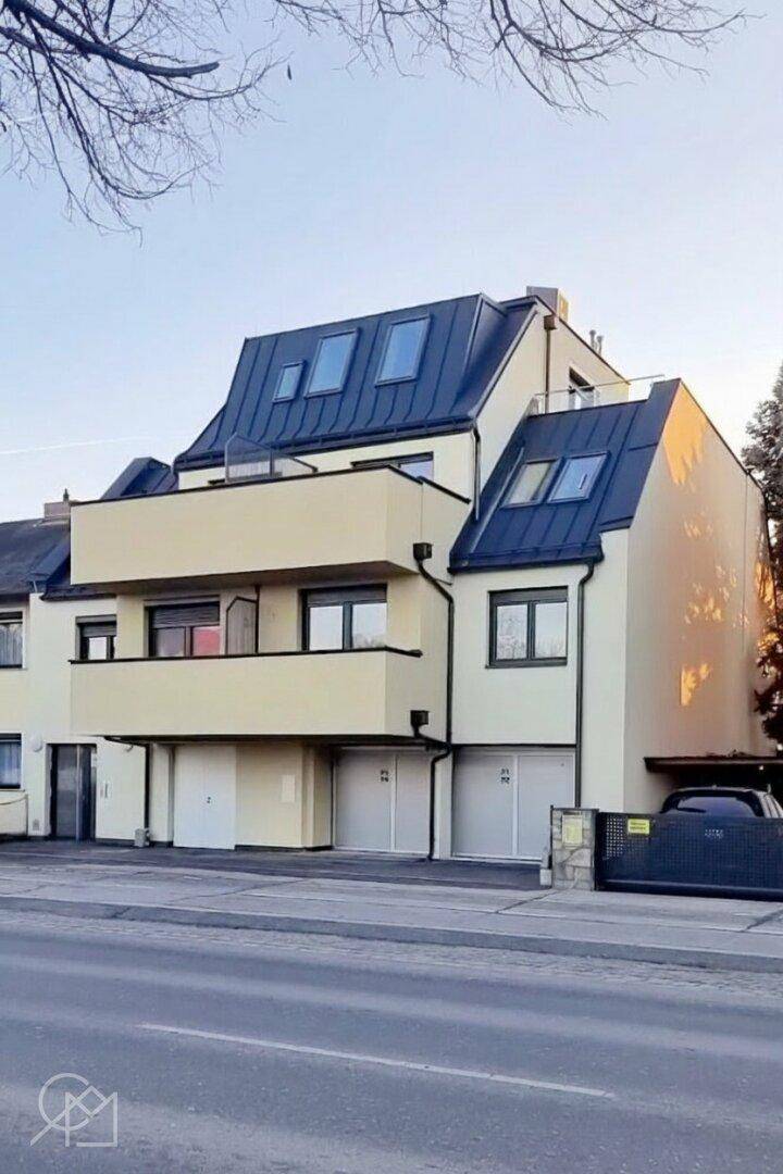 Moderne Wohnanlage mit mehreren Balkonen und Dachfenstern, von der Straße aus gesehen.