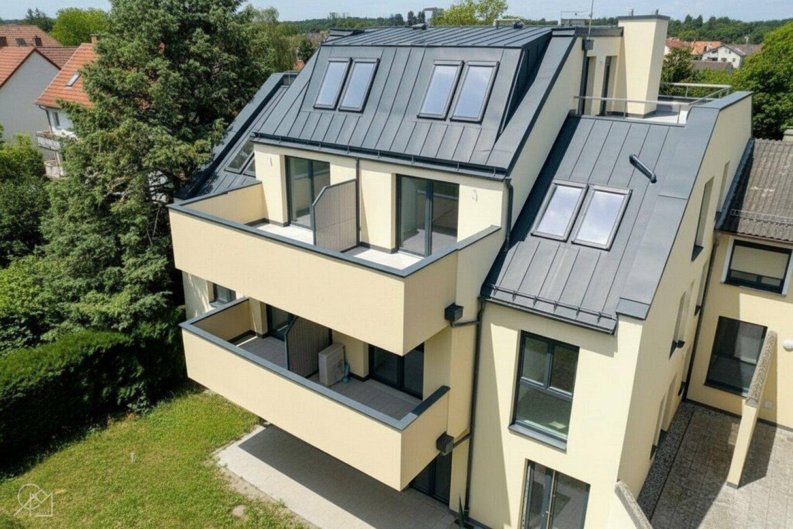 Luftaufnahme einer modernen Wohnanlage mit mehreren Balkonen und Dachfenstern in grüner Umgebung.