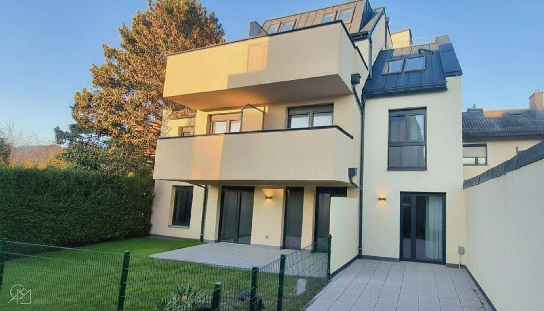 Moderne Wohnanlage mit Balkonen, Terrassen und gepflegtem Gartenbereich bei Sonnenuntergang.