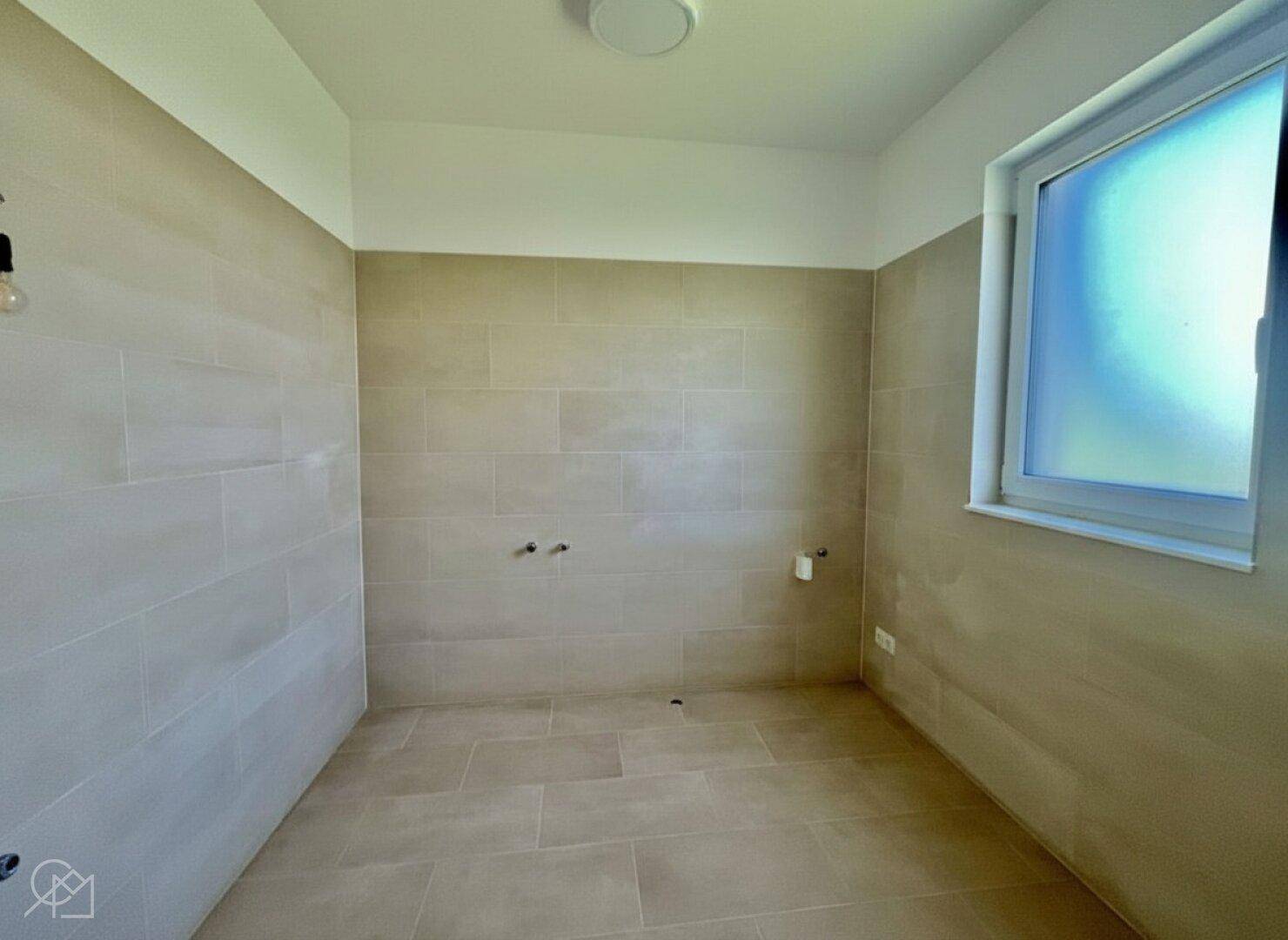 Helles Badezimmer mit beigefarbenen Fliesen und einem Fenster für Tageslicht.