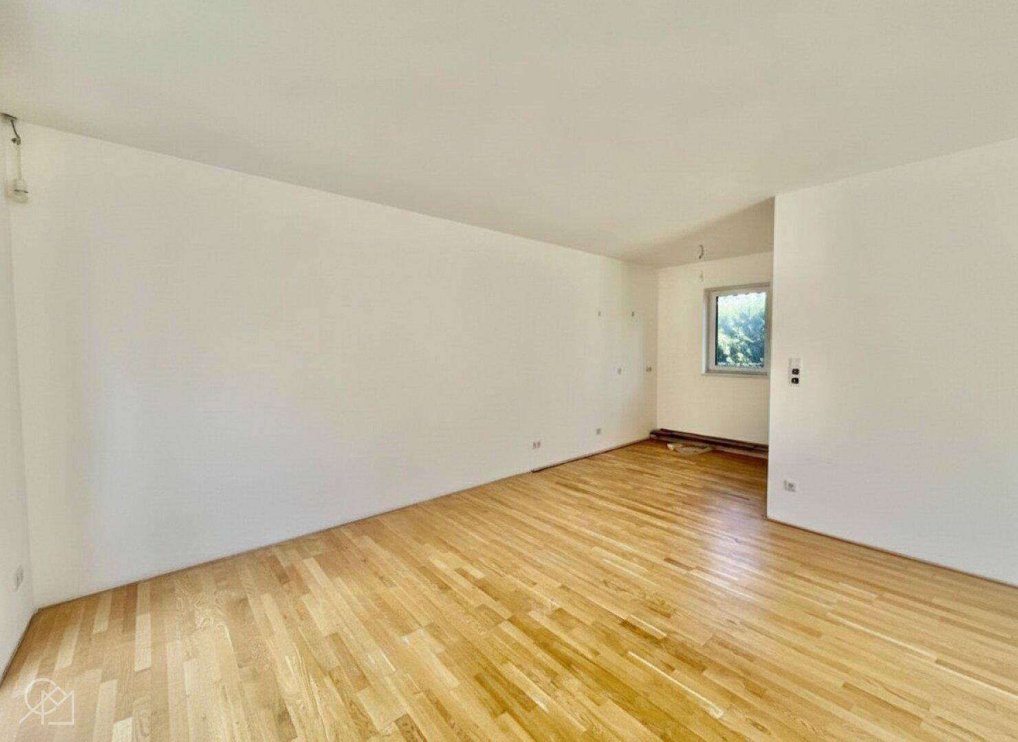 Leerer Raum mit Holzboden und einem Fenster, das viel Tageslicht hereinlässt.