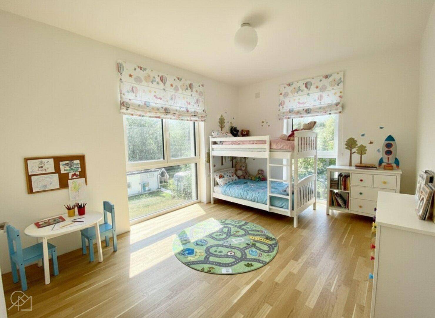 Freundliches Kinderzimmer mit Etagenbett, Holzboden und großen Fenstern zum Garten.