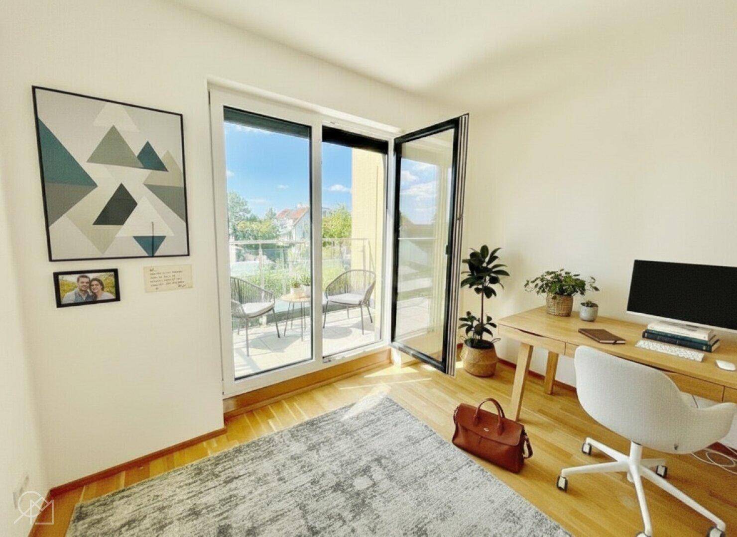 Modernes Büro mit Schreibtisch, Holzboden und Zugang zu einem sonnigen Balkon.
