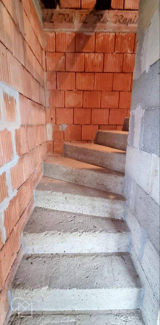 Unfertige Betontreppe in einem Rohbau mit Ziegelwänden.