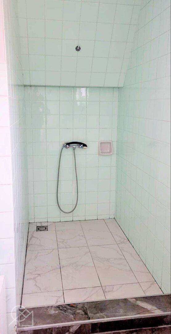 Einfacher Duschbereich mit hellgrünen Fliesen und Handbrause.