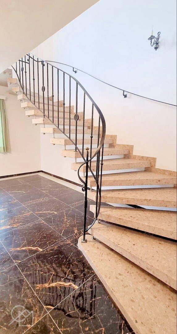 Geschwungene Treppe mit schmiedeeisernem Geländer und Steinstufen.