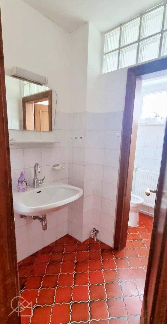 Badezimmer mit Terrakotta-Fliesen, Waschbecken und Glasbaustein-Fenster.
