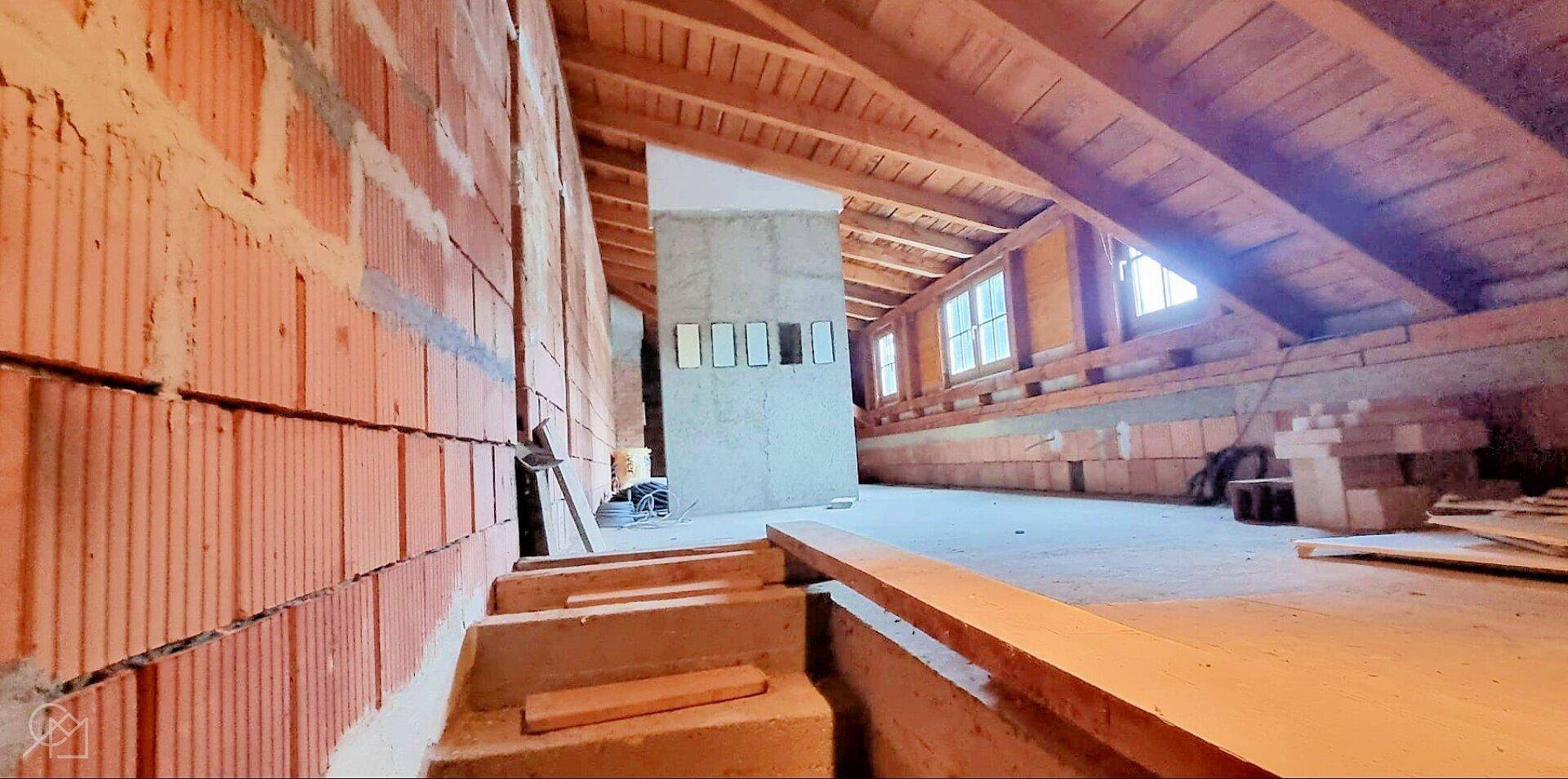 Unfertiger Dachboden mit sichtbaren Holzbalken und Ziegelwänden.