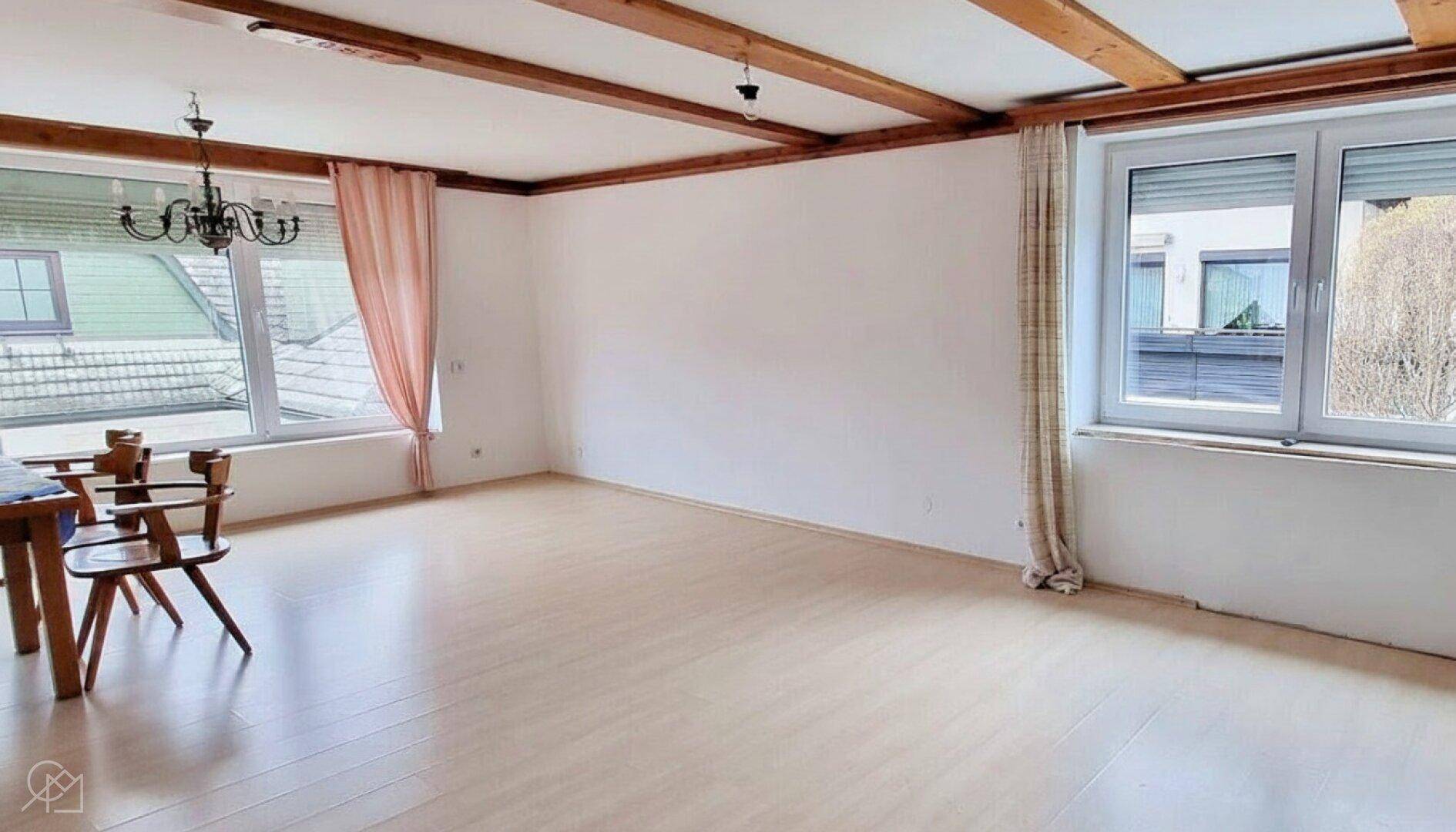 Geräumiges Wohnzimmer mit sichtbaren Holzbalken und großen Fenstern.