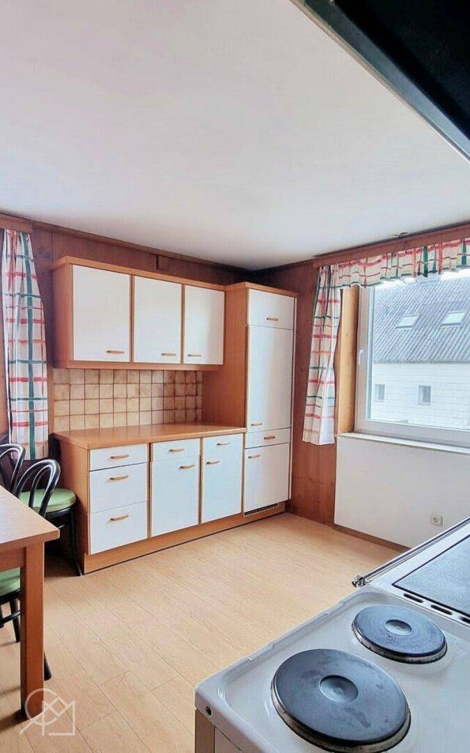 Küche mit älteren Einbauschränken, Elektroherd und Holzvertäfelung.