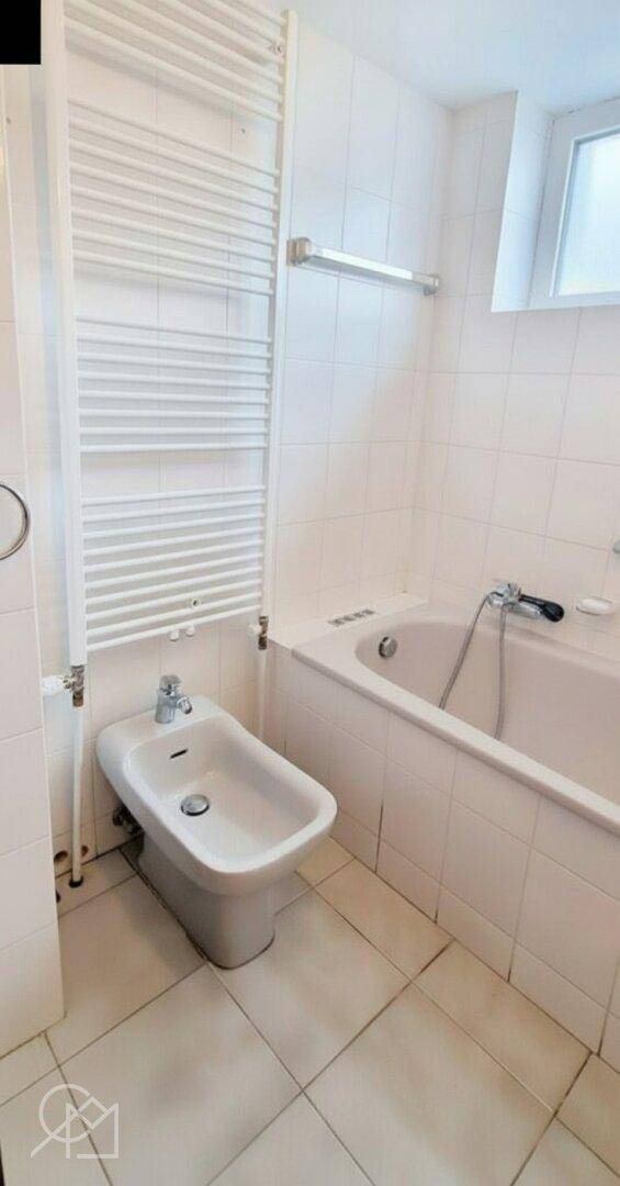 Badezimmer mit Badewanne, Bidet, Handtuchheizkörper und weißen Fliesen.
