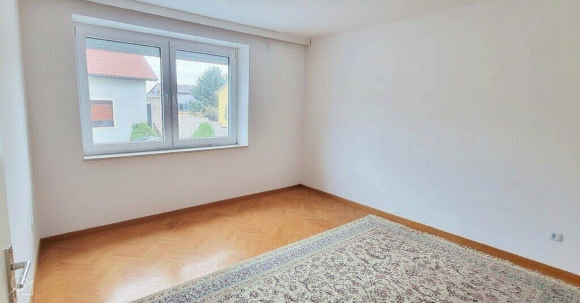 Unmöbliertes Zimmer mit Parkettboden und Blick ins Grüne.