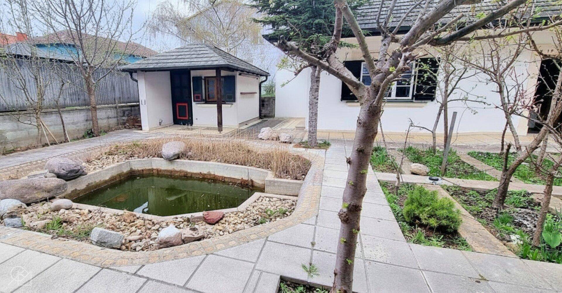Garten mit Teich, Bäumen und einem kleinen Gartenhaus.