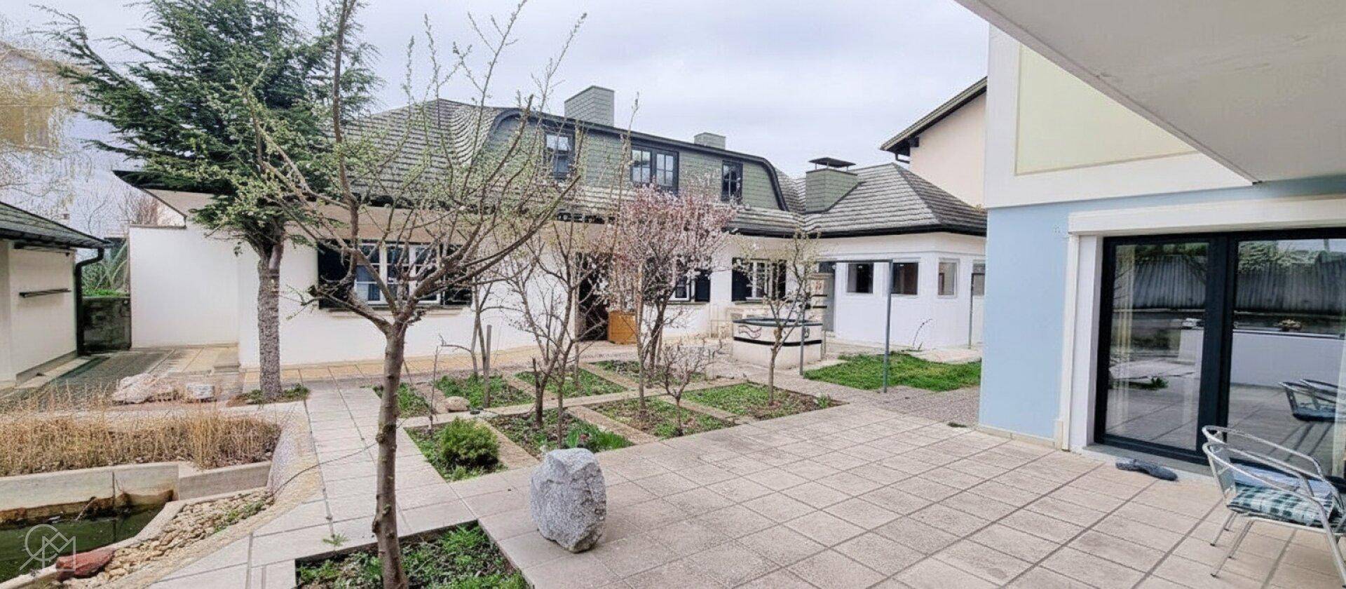 Gartenbereich mit Teich, Bäumen und gepflasterter Terrasse.