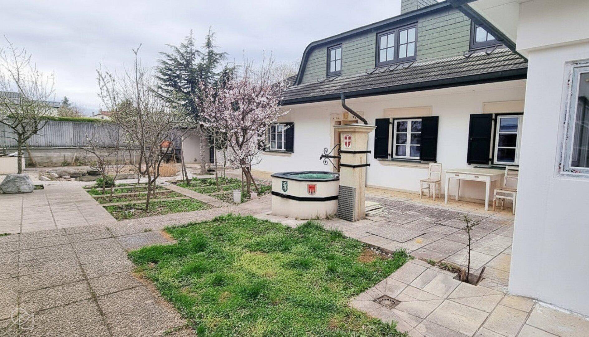 Garten mit Zierbrunnen, gepflastertem Bereich und Sitzgelegenheiten.