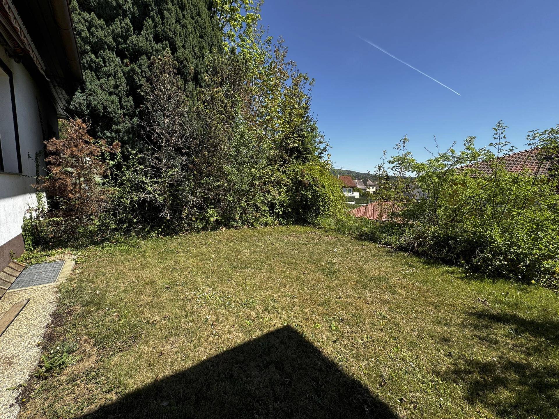 Gepflegte Rasenfläche neben dem Haus mit Blick auf die umliegende Landschaft und Häuser.