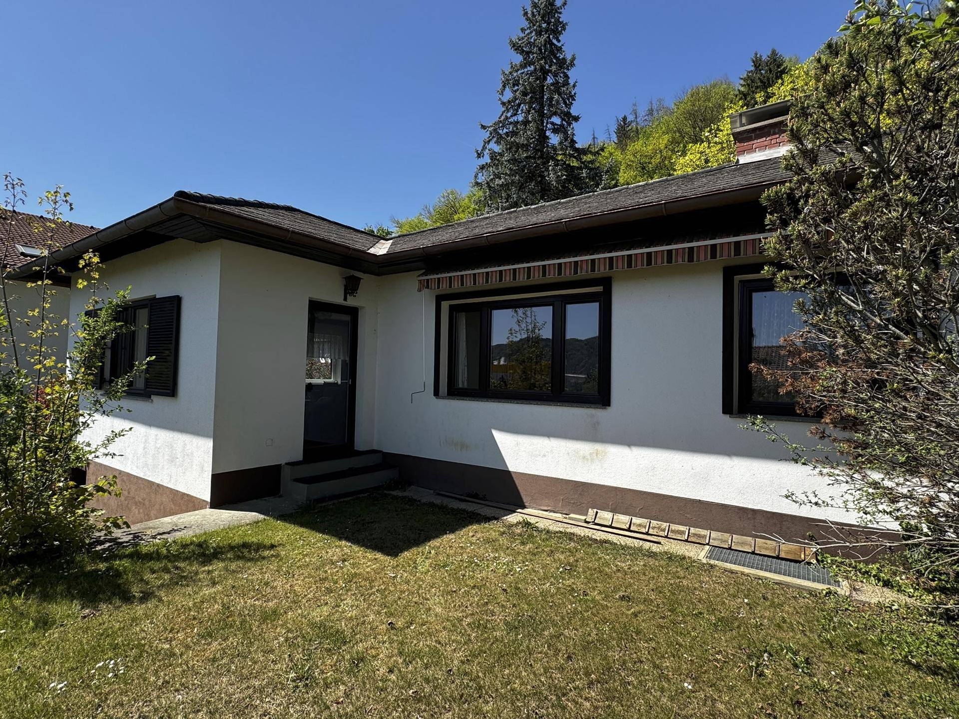 Seitenansicht des Hauses mit Fenstern und einer kleinen Rasenfläche im Vordergrund.