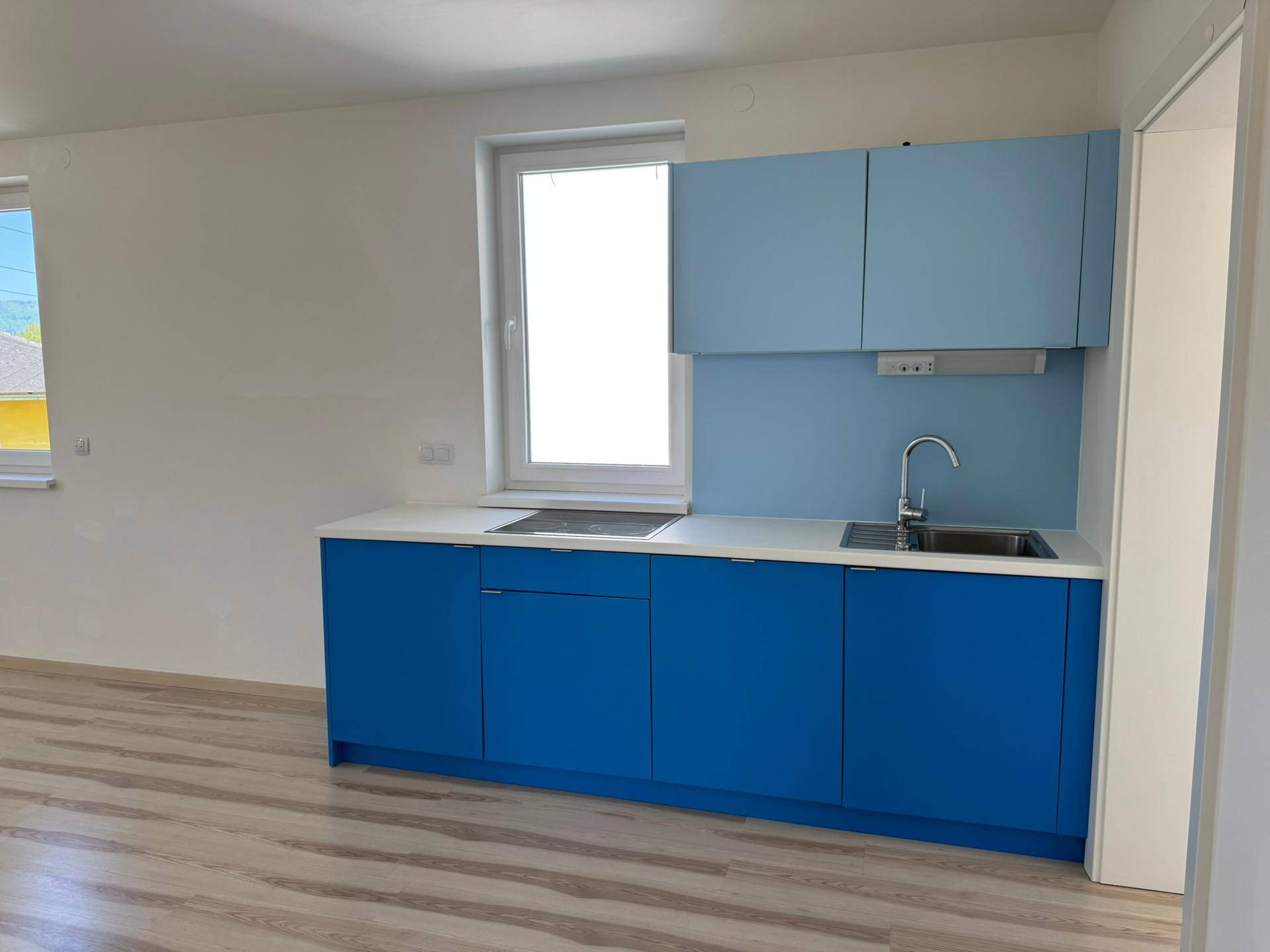 Kleine, funktionale Küche mit blauen Schränken, weißer Arbeitsplatte und einem Fenster für Tageslicht.