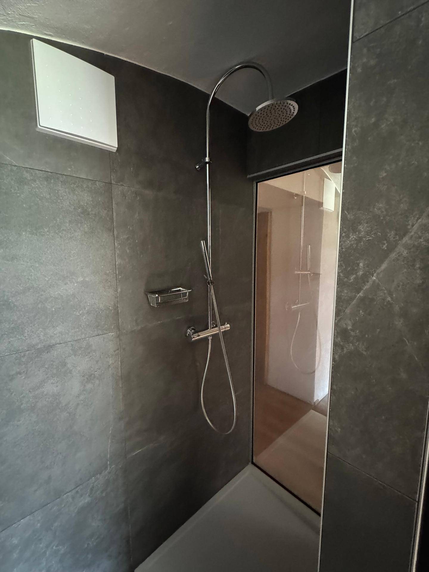 Modernes Badezimmer mit dunklen Fliesen und einer Regendusche für ein entspannendes Duscherlebnis.