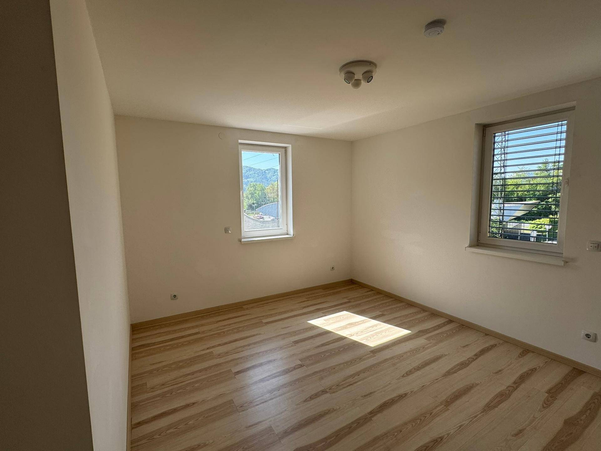 Helles Schlafzimmer mit Holzboden und zwei Fenstern, die einen Blick auf die Berge ermöglichen.