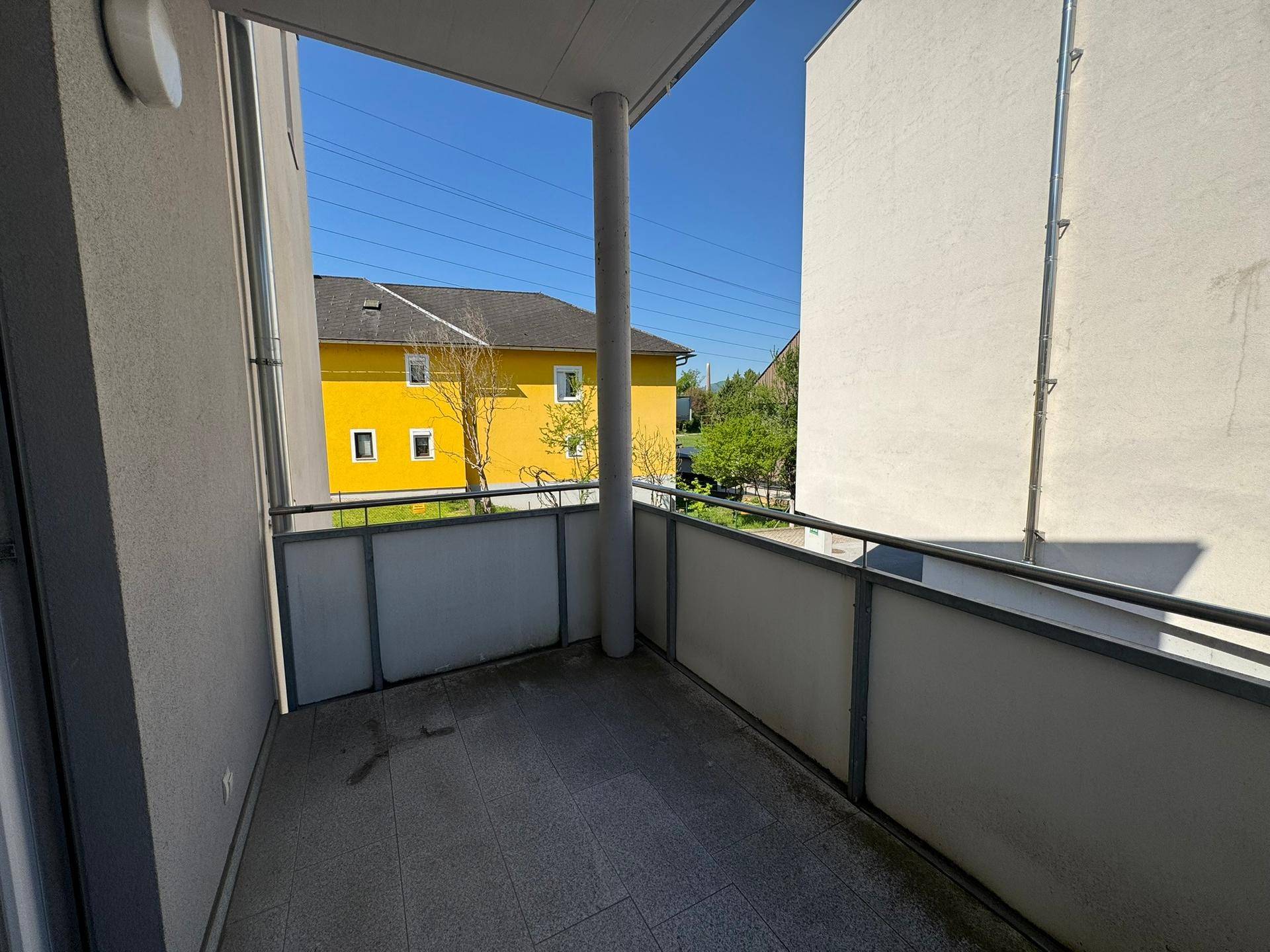 Kleiner Balkon mit Fliesenboden und Blick auf die umliegenden Gebäude und Grünflächen.