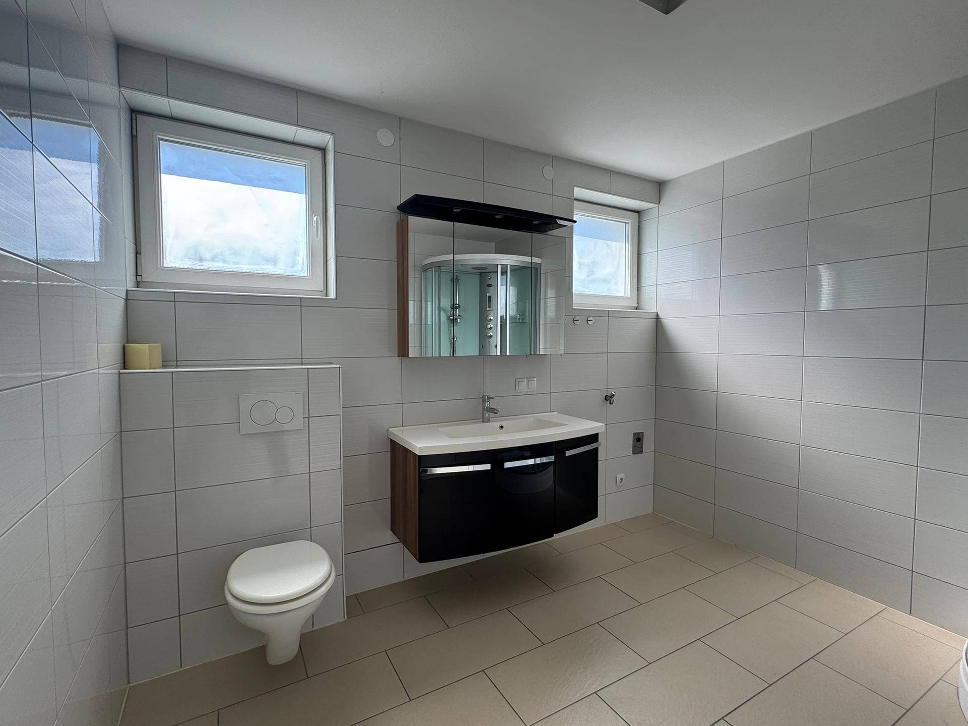 Geräumiges Badezimmer mit Doppelwaschbecken, Hänge-WC und zwei Fenstern.