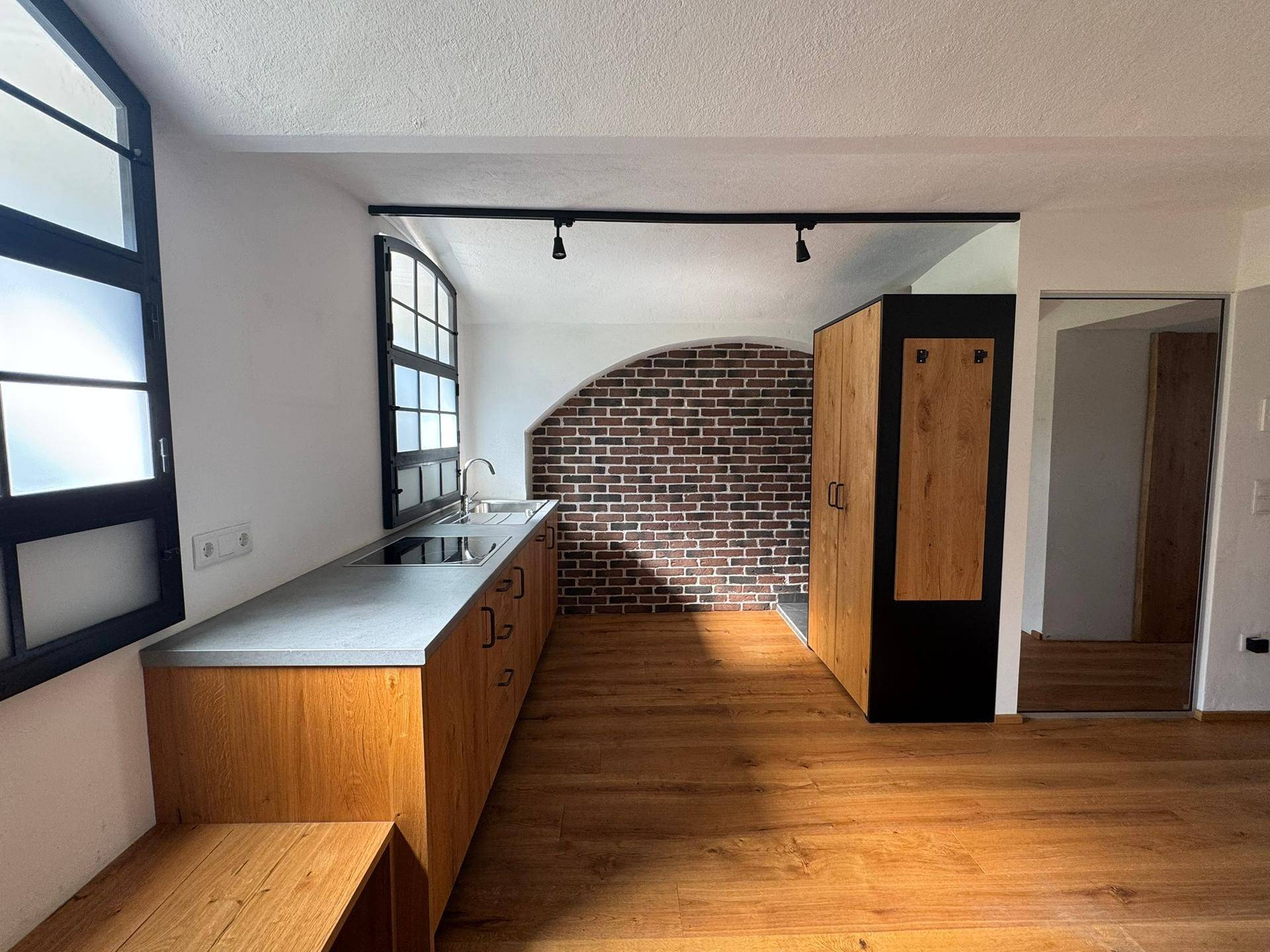 Moderne Küche mit Holzelementen, freiliegender Ziegelwand und großen Fenstern.