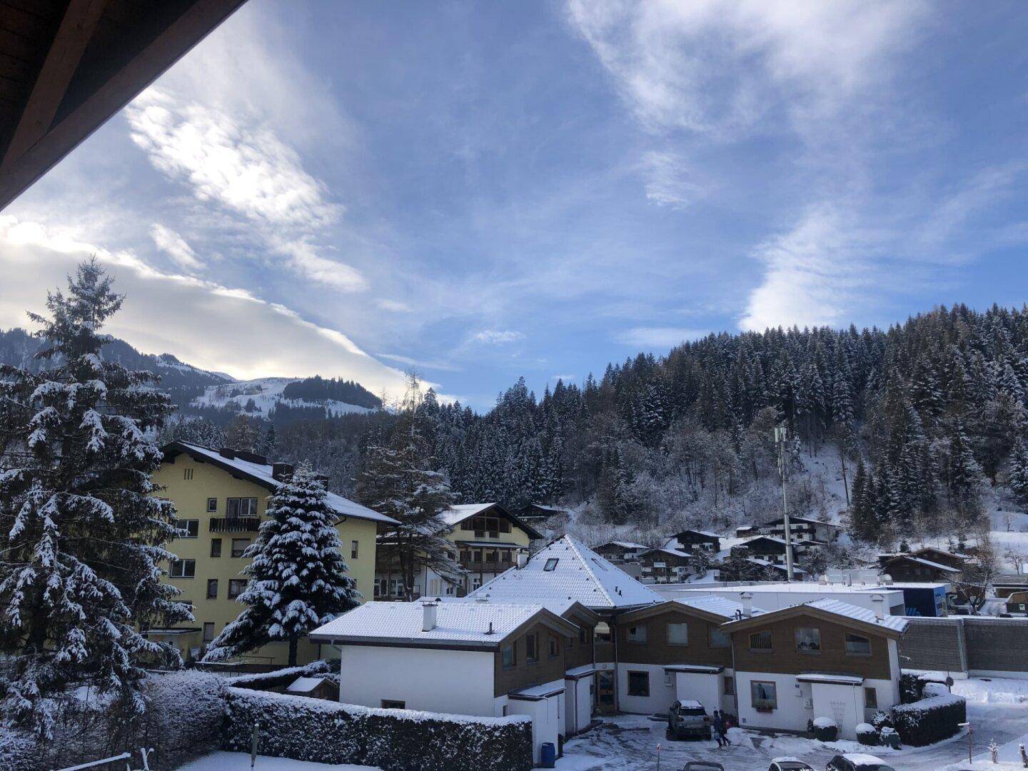 Winterliche Landschaft mit schneebedeckten Häusern und Bergen unter blauem Himmel.