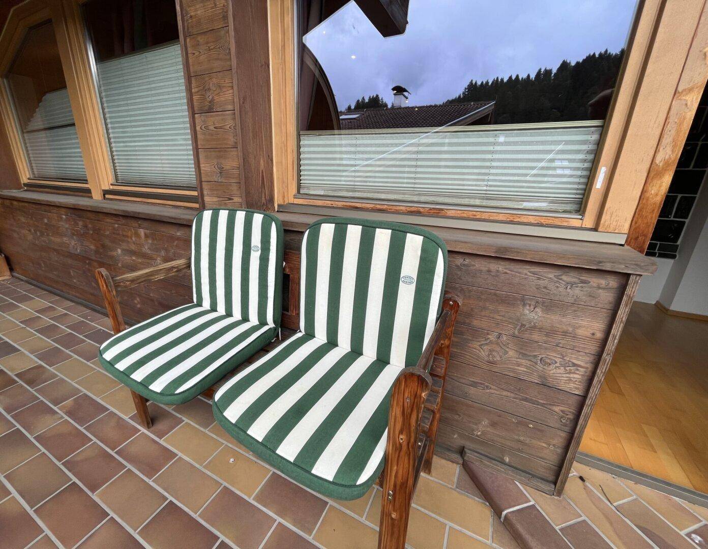 Balkon mit zwei Stühlen und gestreiften Polstern, umgeben von Holzverkleidung.