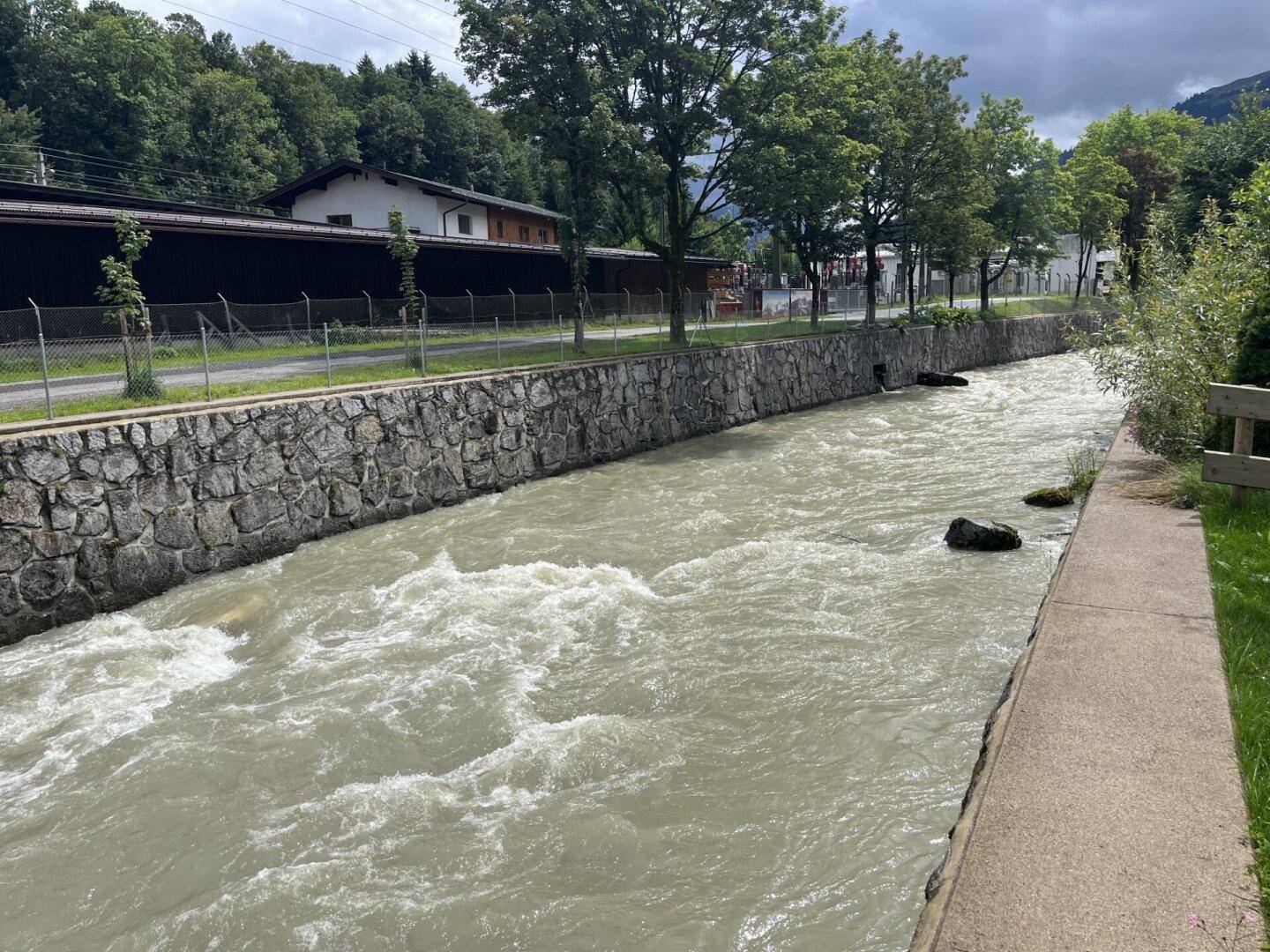 Fließender Fluss mit steinernen Ufern und grüner Vegetation.