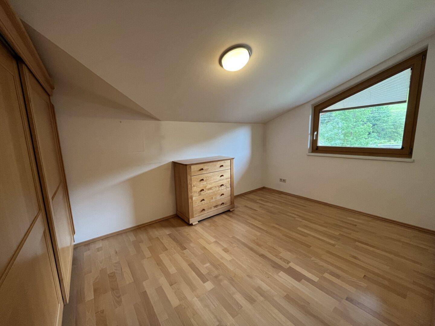 Helles Schlafzimmer mit Dachschräge, Holzboden und Kommode.