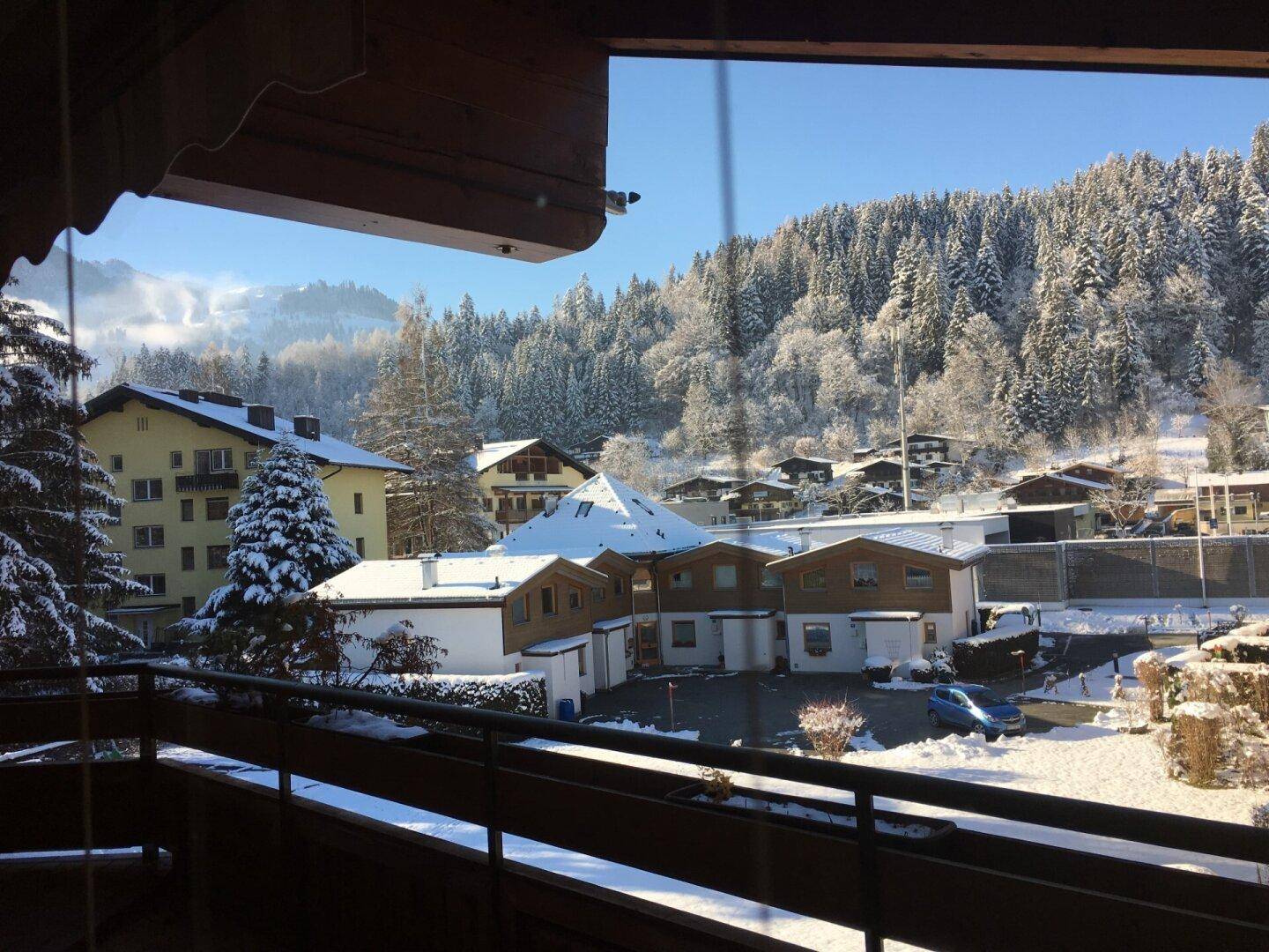 Sonniger Balkon mit Blick auf schneebedeckte Häuser und Berge.