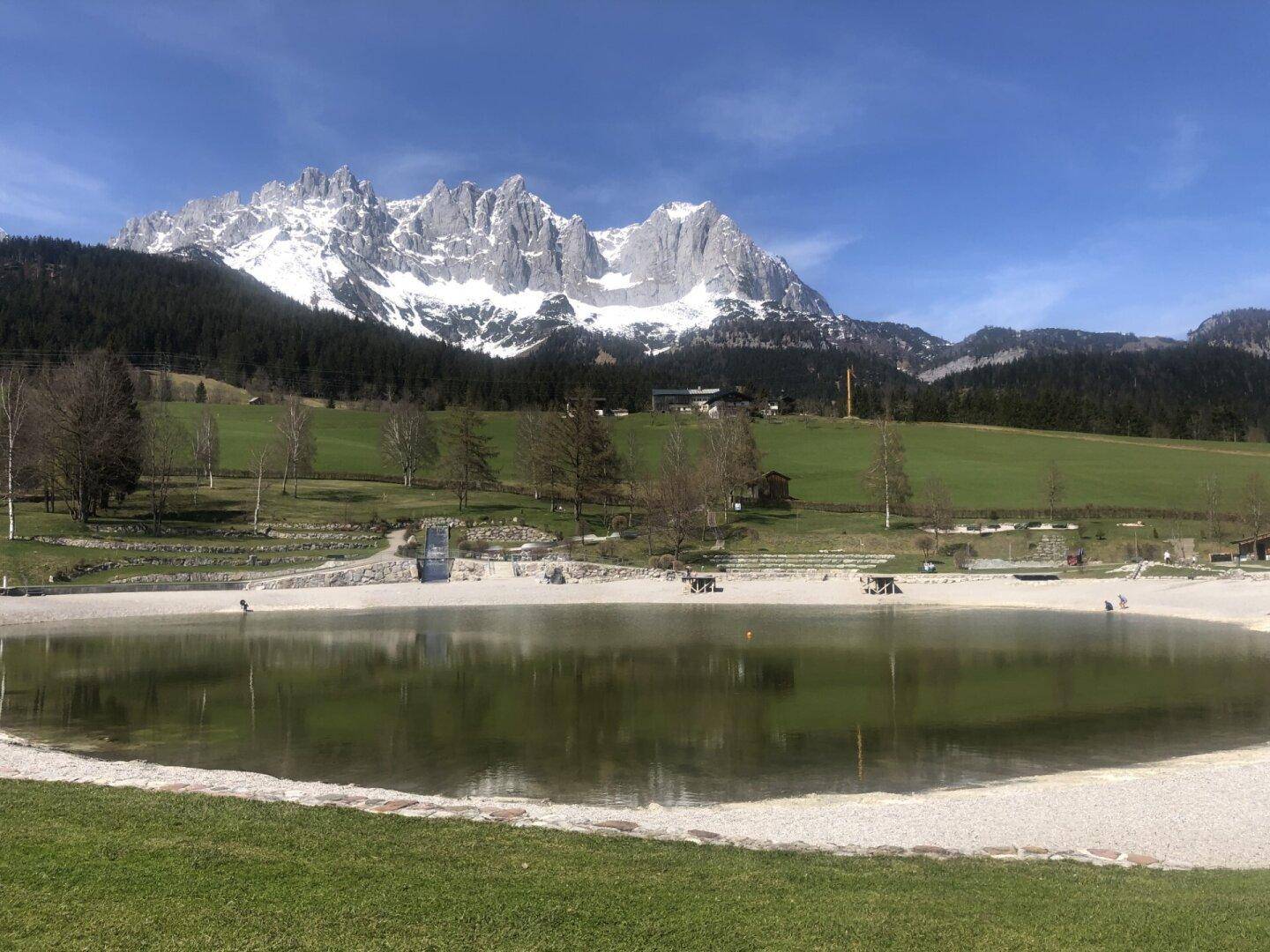 Malerischer See mit Sandstrand und majestätischem Alpenpanorama im Hintergrund.