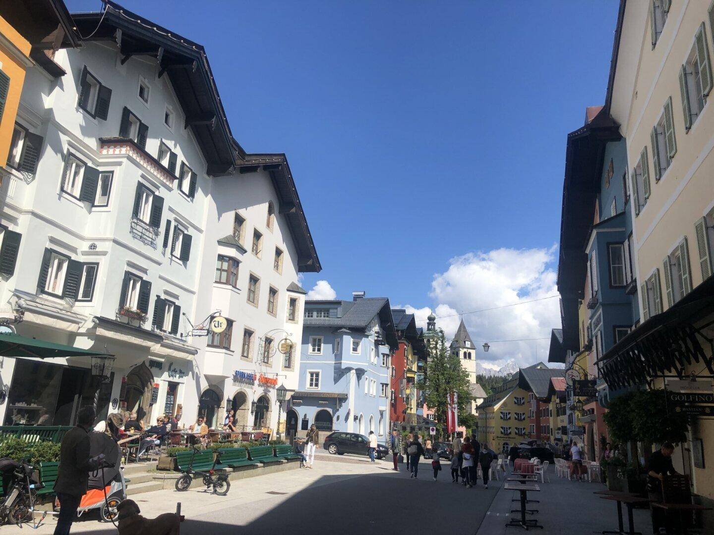 Belebte Gasse in einer malerischen Stadt mit traditionellen Gebäuden und blauem Himmel.