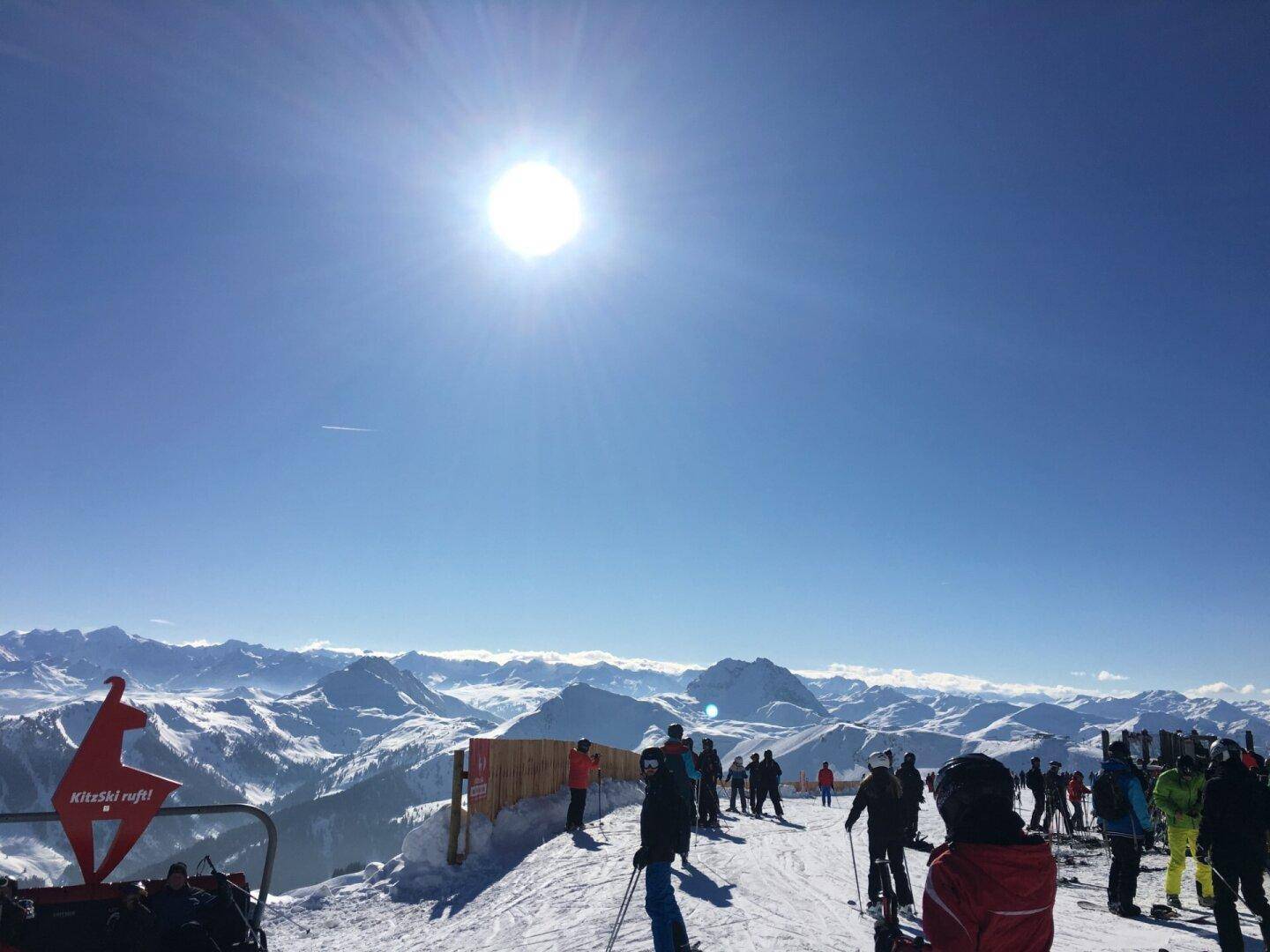 Sonniger Panoramablick über verschneite Skipisten und weite Bergketten mit vielen Skifahrern.