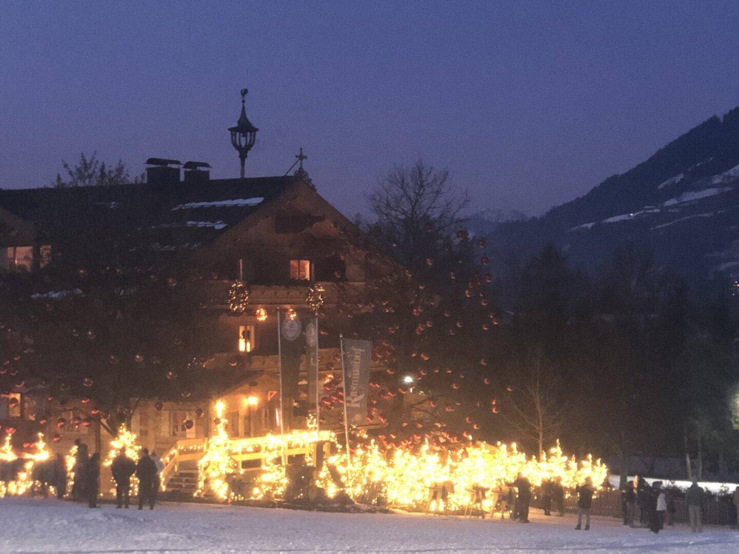 Historisches Gebäude festlich beleuchtet in einer verschneiten Winternacht mit Bergblick.