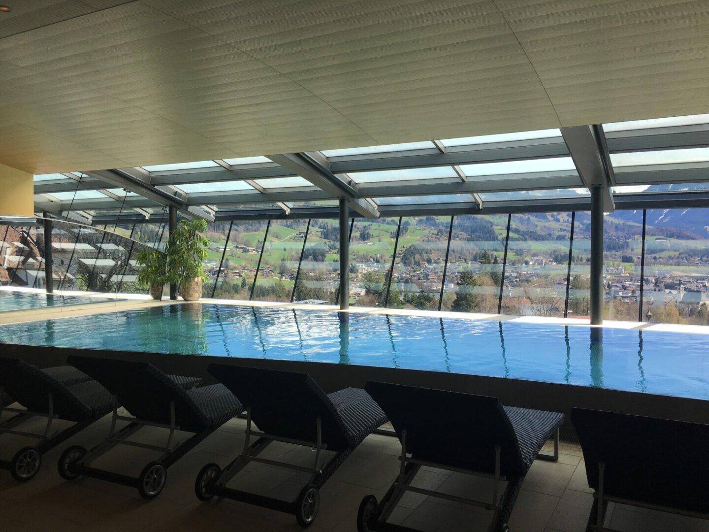 Hallenbad mit Liegestühlen und Panoramafenstern mit weitem Blick über das Tal und die Berge.