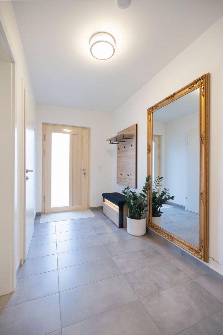 Geräumiger Flur mit grauen Fliesen, einer Garderobe und einem großen, verzierten Spiegel.