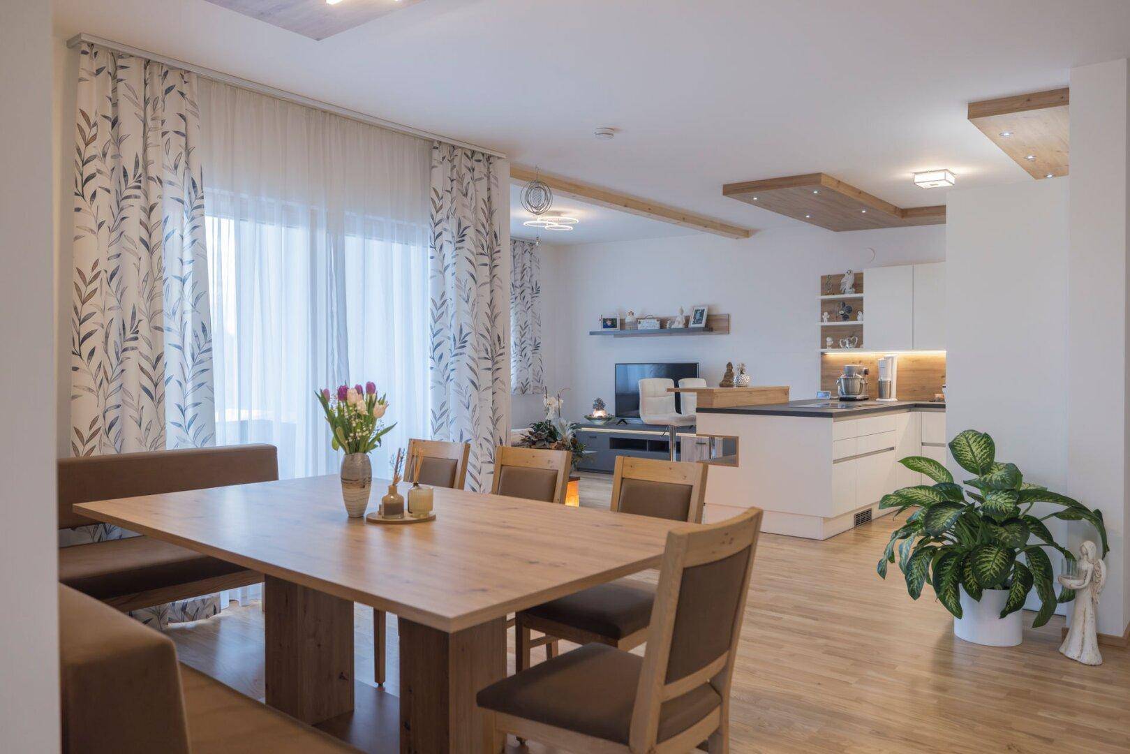 Offener Wohn-Essbereich mit Holztisch, Eckbank und Blick auf die moderne Küche und den Wohnbereich.