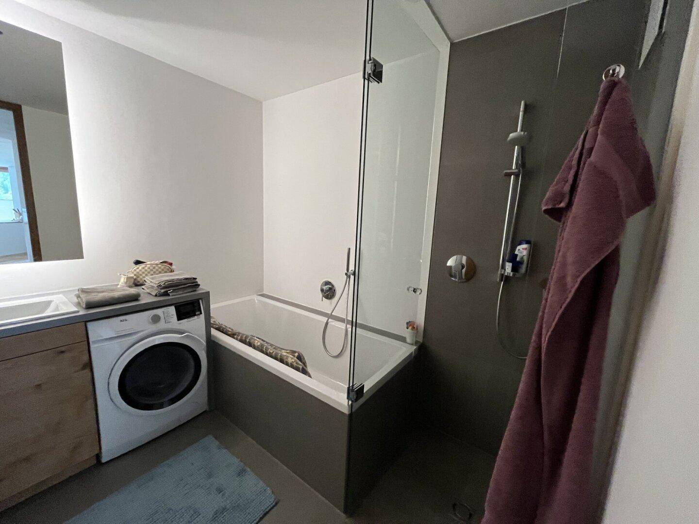 Modernes Badezimmer mit Badewanne, Dusche, Waschbecken und Waschmaschine.
