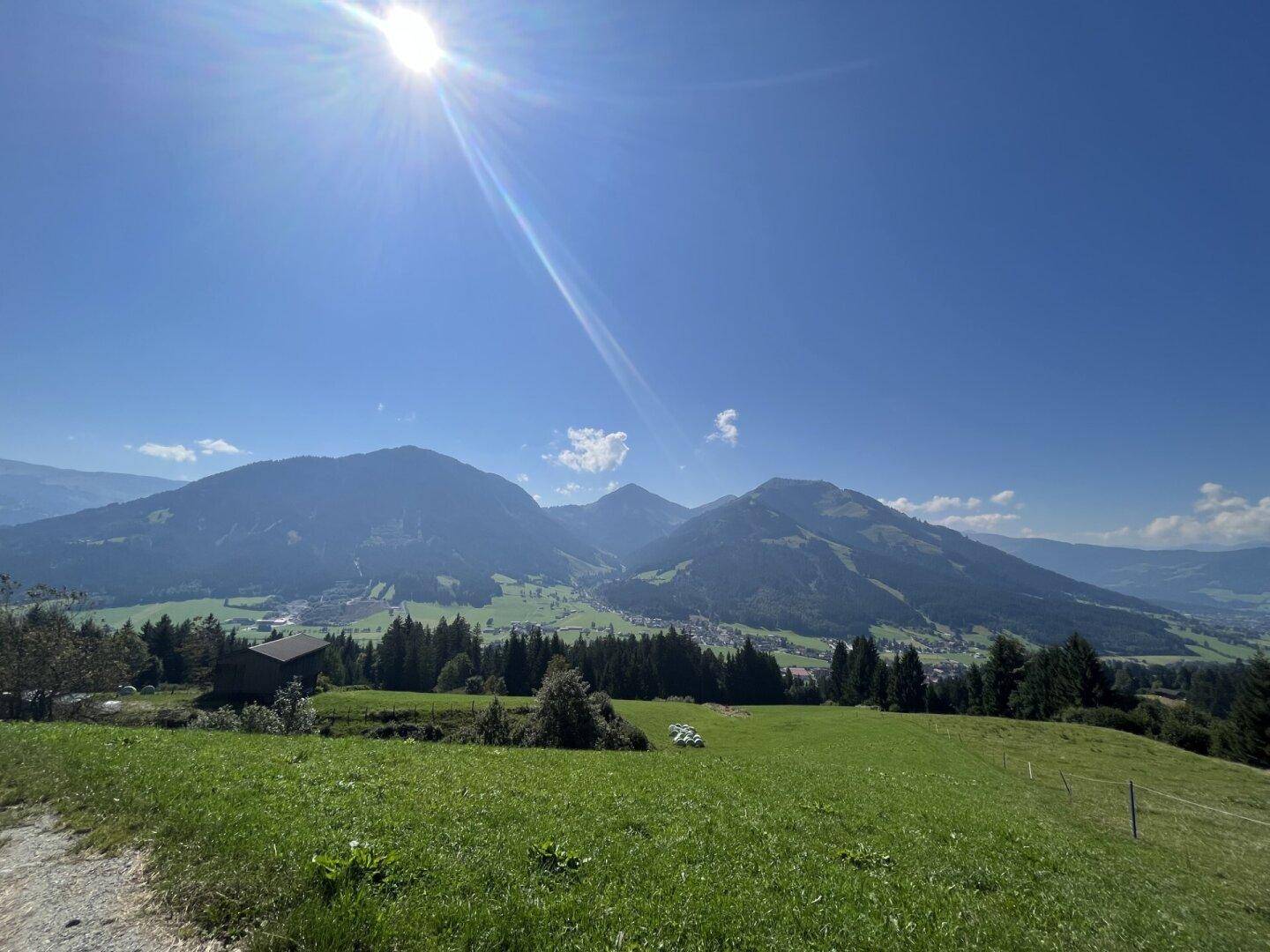 Weitläufige grüne Landschaft mit Hügeln, Wäldern und Bergen unter strahlendem Sonnenschein.