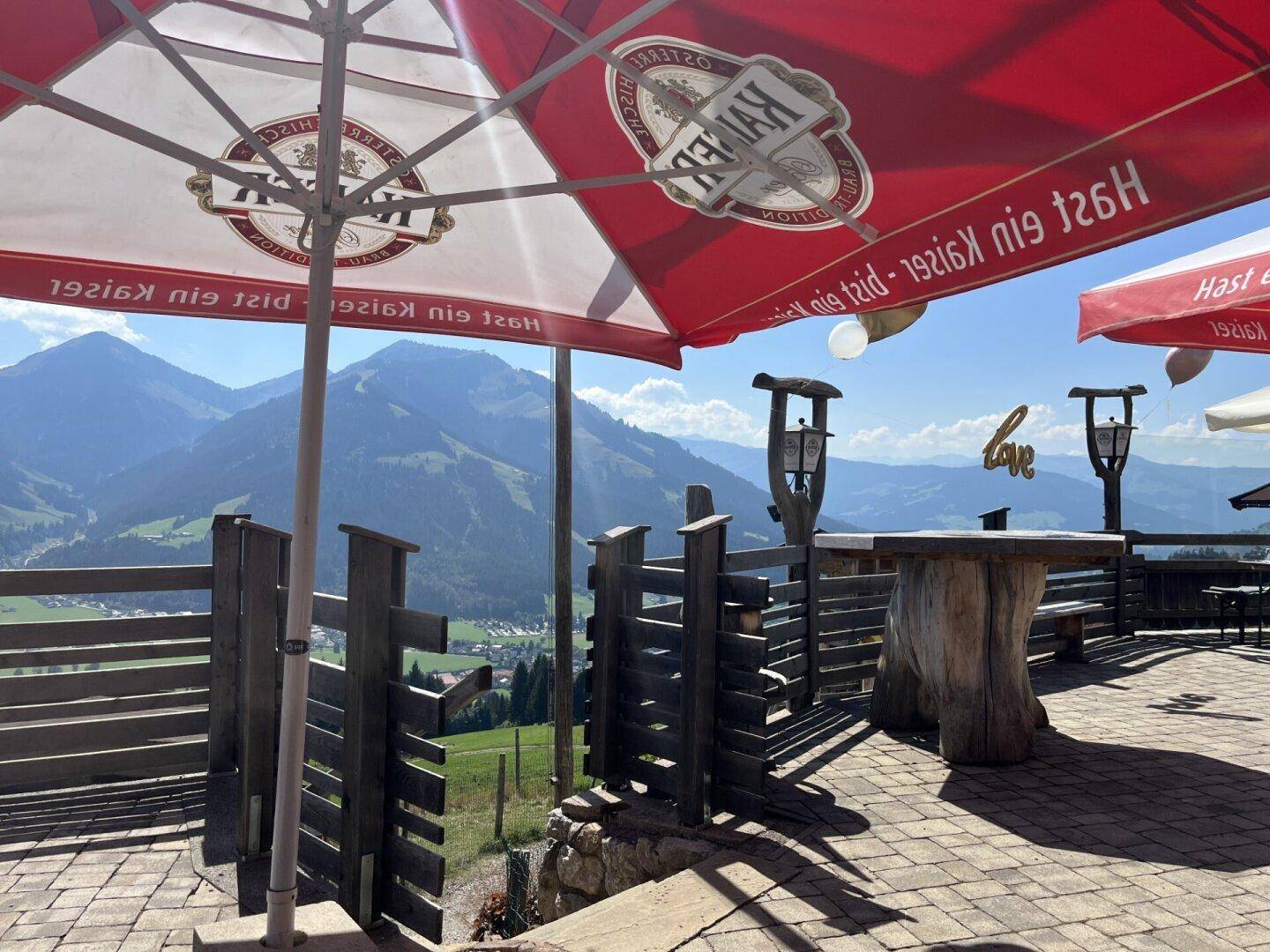 Gemütlicher Außenbereich mit Holztischen und Bergblick unter großen Sonnenschirmen.