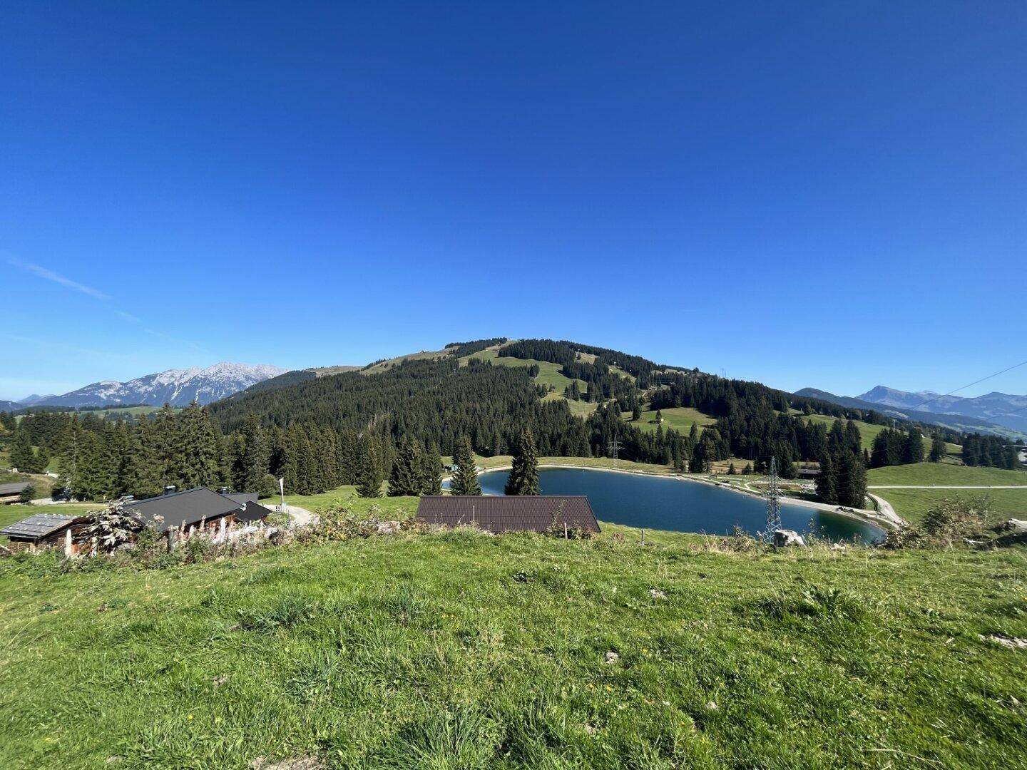 Panoramablick auf eine Berglandschaft mit grünen Wiesen, Wäldern und einem Stausee.