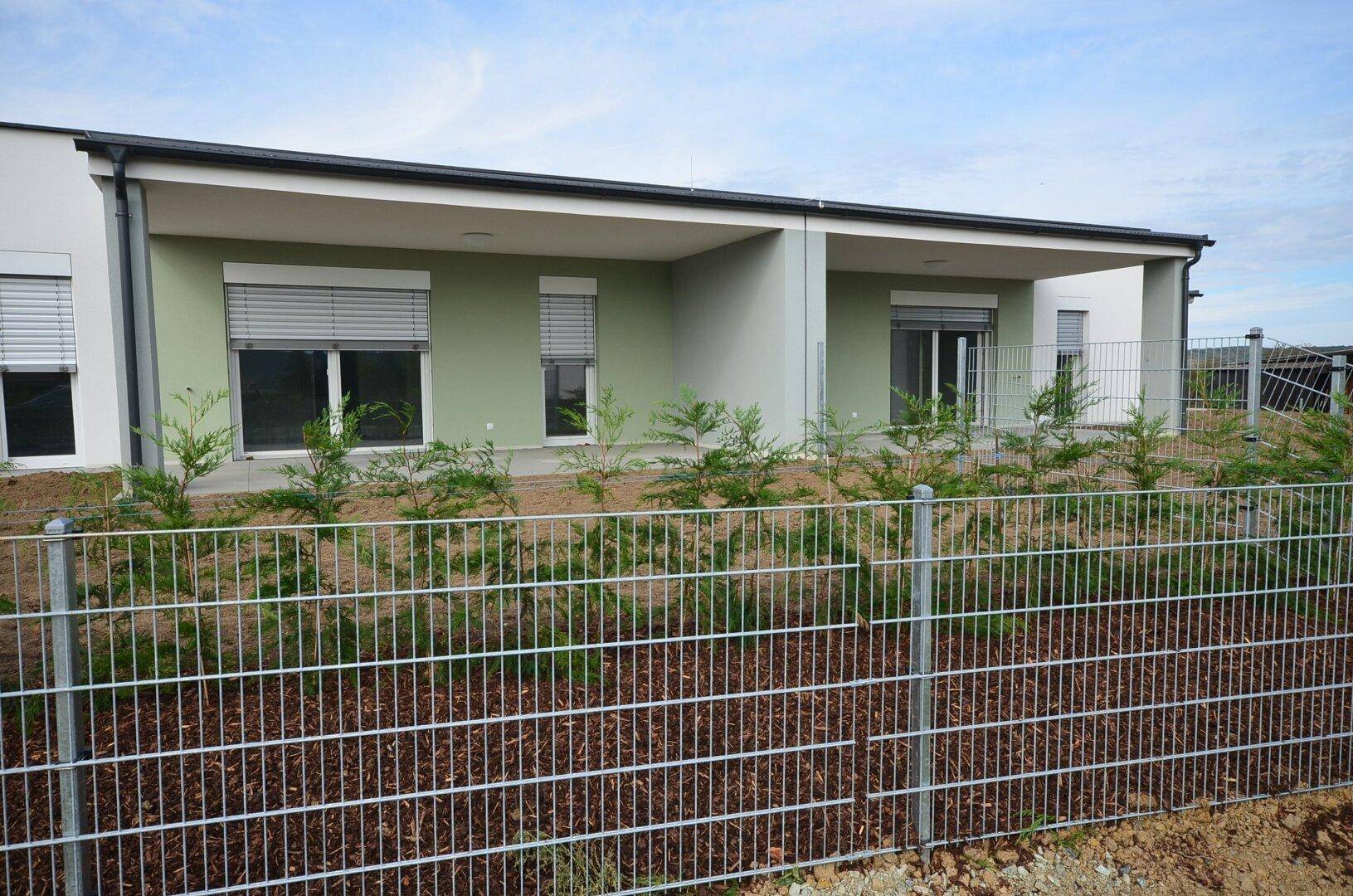 Rückseite von Neubauten mit Terrassen und einem noch ungestalteten Gartenbereich, umgeben von einem Zaun.