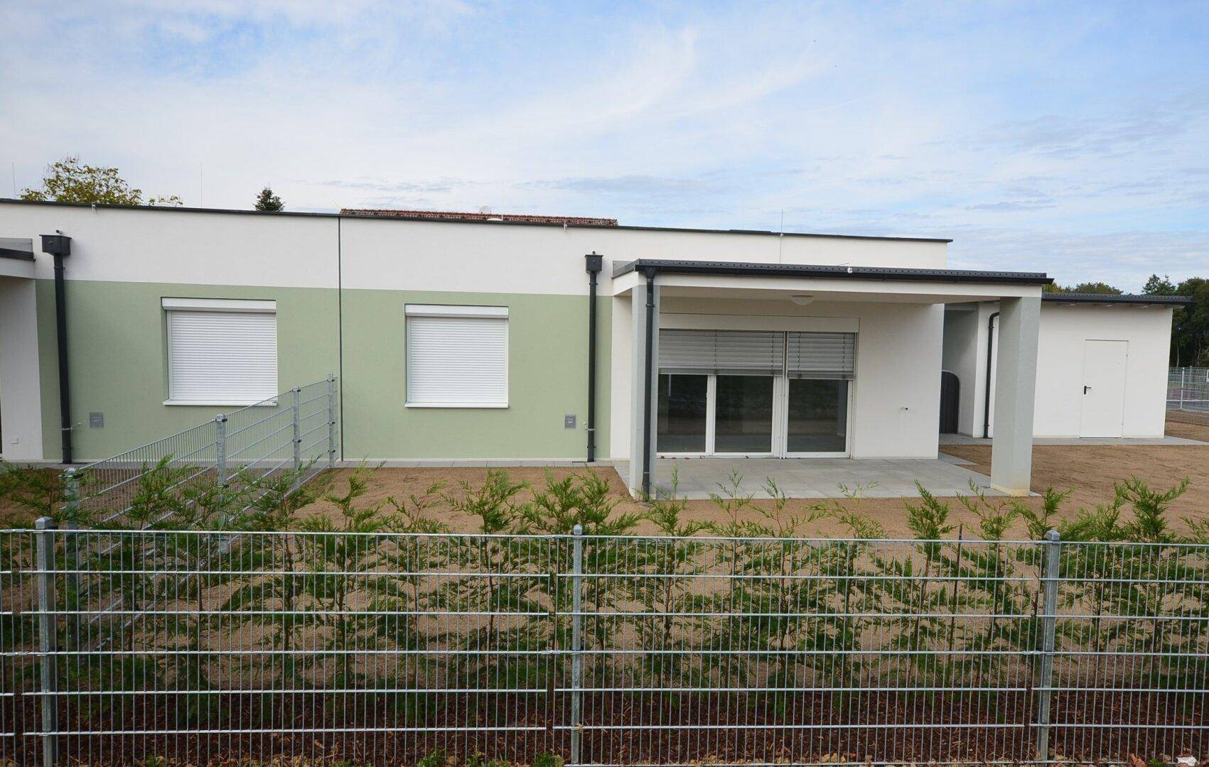 Rückseite von Neubauten mit Terrassen und einem noch ungestalteten Gartenbereich, umgeben von einem Metallzaun.