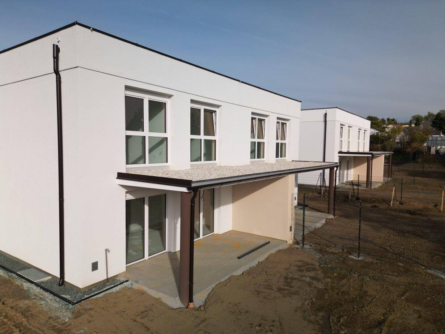 Moderne Reihenhäuser im Bau mit großen Fenstern und zukünftigen Terrassenbereichen.